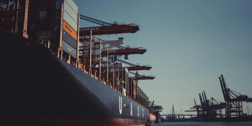 A large cargo ship docked at Hamburg Harbor, cranes loading containers under a clear sky.